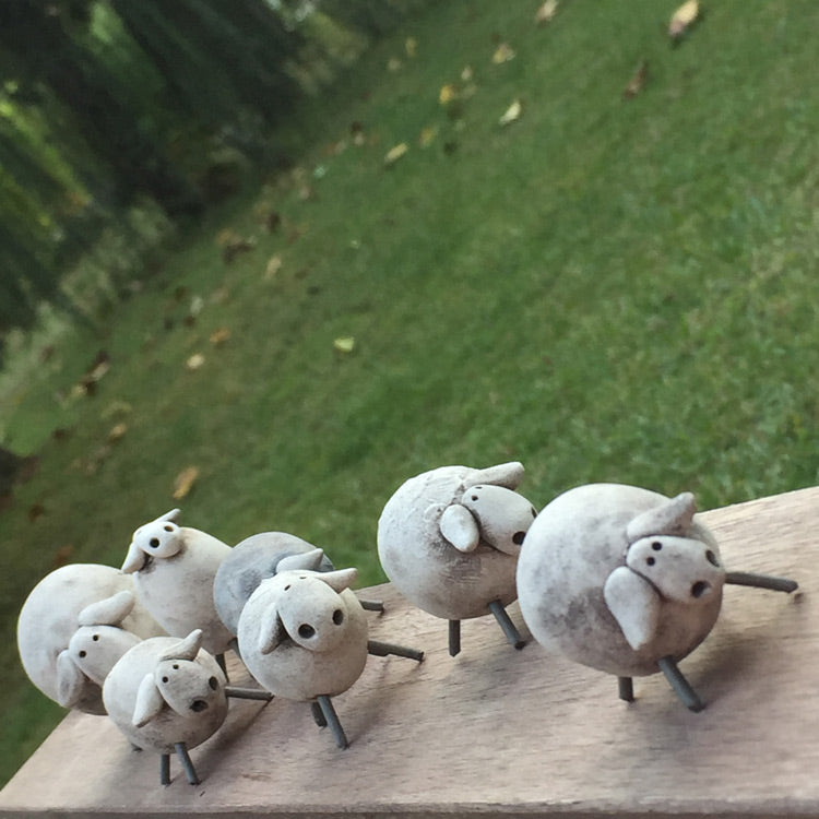 Bahcedeki masanin kenarinda duran gri seramik koyun biblolari_Grey ceramic sheep trinkets on the garden table