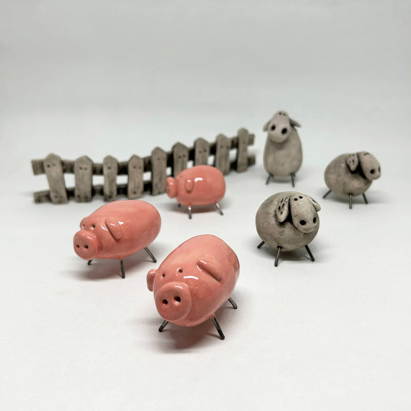 Citin onunde duran pembe seramik domuzlar ve gri koyunlar_Small pink ceramic piggies and grey sheep in front of the fence