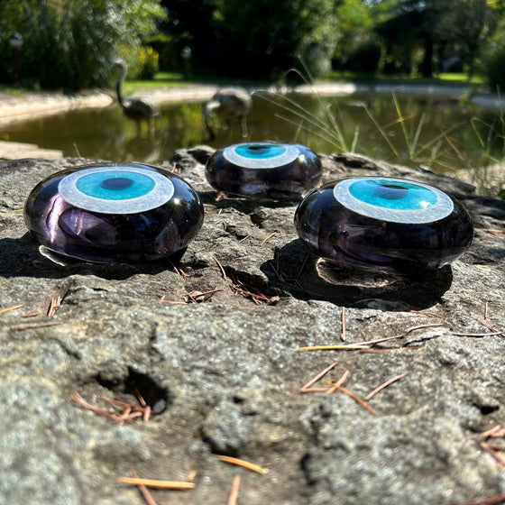 Golet yaninda kayada turkuaz koyu gri cam nazarliklar_Dark grey transparent evil eye beads on the pond rock