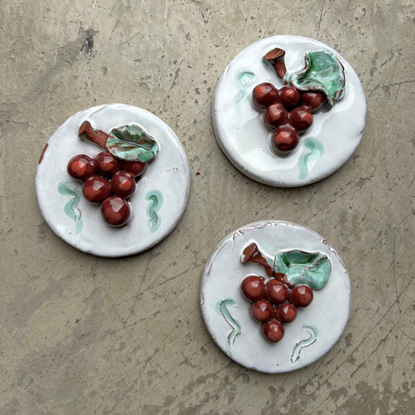Gri zeminde uc adet kirmizi uzum kabartmali beyaz dairesel seramik sus_Three white circular ceramic ornaments embossed with red grapes
