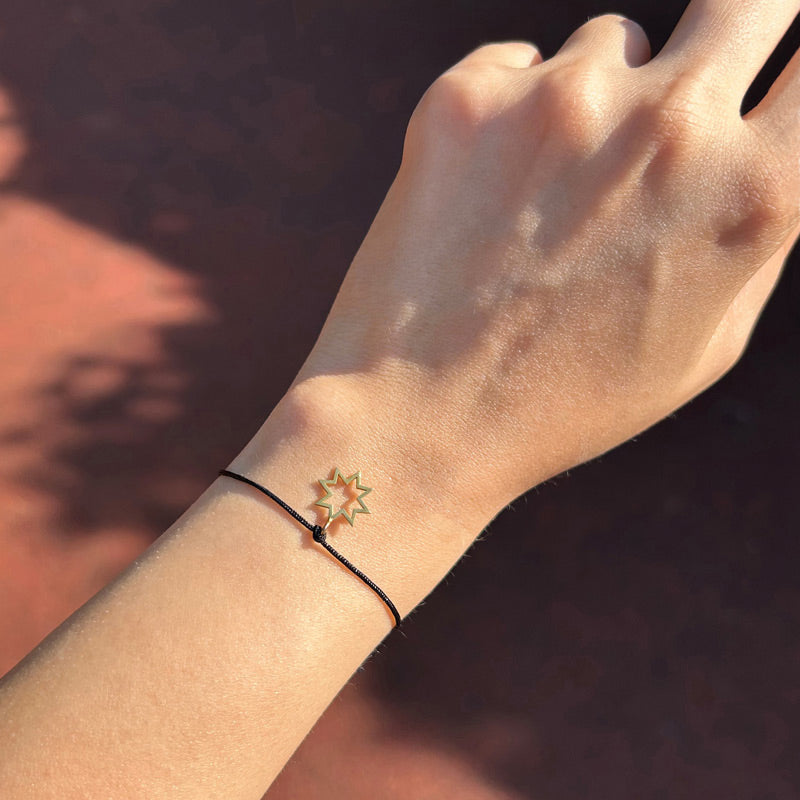 Gunesli bir gunde kolda duran yildiz motfli siyah ipli bileklik_A black string bracelet with a star motif on the arm on a sunny day