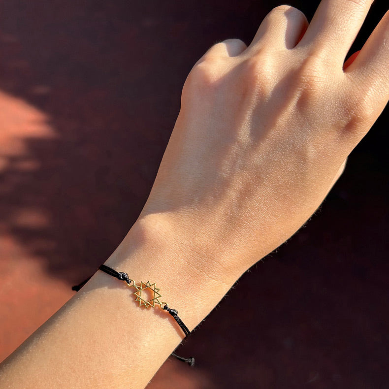 Gunesteki kadin kolunda altin kaplama yildizli siyah ipli bileklik_Black string bracelet with eight pointed star on woman arm