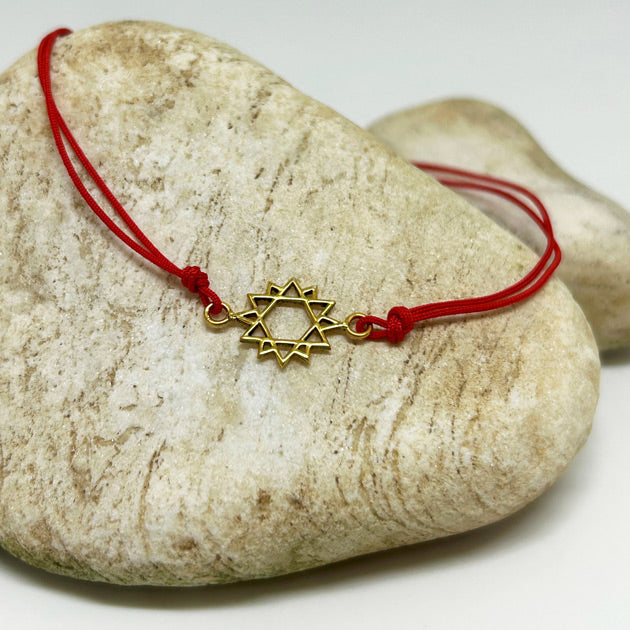 Tas ustunde duran altin kaplama on iki koseli yildiz motifli kirmizi ipli bileklik_Red string bracelet with a gold-plated twelve-pointed star motif on a stone