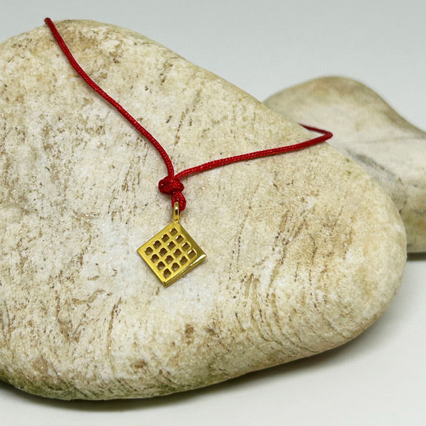 Tas ustunde duran bereket sembolu Anadolu Motifli kirmizi ipli bileklik_Red string bracelet with Anatolian Motif symbolizing fertility on a stone