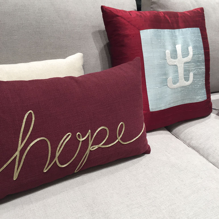 Acik gri kanepede elibelinde motifli bordo ve hope yazan acik gri kirlent_Burgundy colored cushion with hands on hips motif beside a light grey cushion with hope text on a light grey