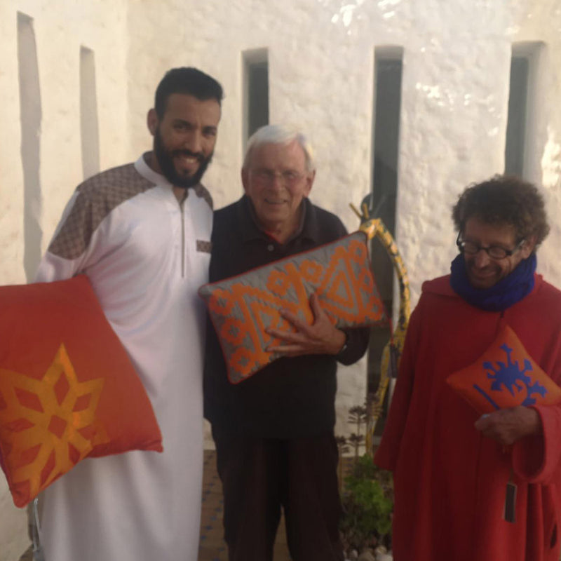 Bir Fas evinin onunde kucaklarinda yastiklarla uc kisi_Three people holding pillows in front of a Moroccan house