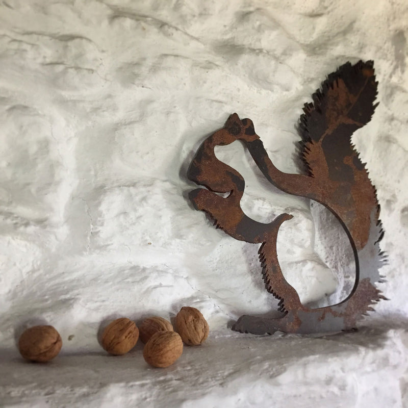 Fonda beyaz tas duvar ile onunde cevizler olan metal sincap_Metal squirrel with walnuts in front with a white stone wall background