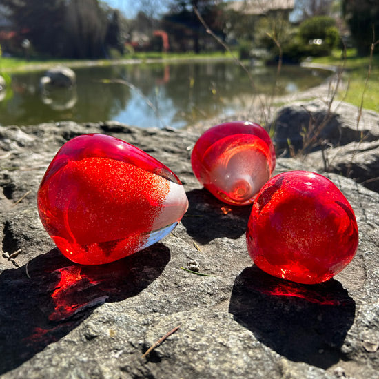 Golet kenarindaki kayanin ustunde uc adet kirmizi cam nar tanesi_Three red glass pomegrante seeds on the rock by the pond
