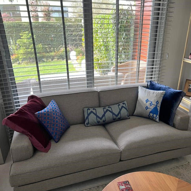 Panjurlu pencerenin onundeki gri kanepede bordo gri ve mavi yastiklar_Burgundy red blue and grey cushions on a grey sofa in the living room