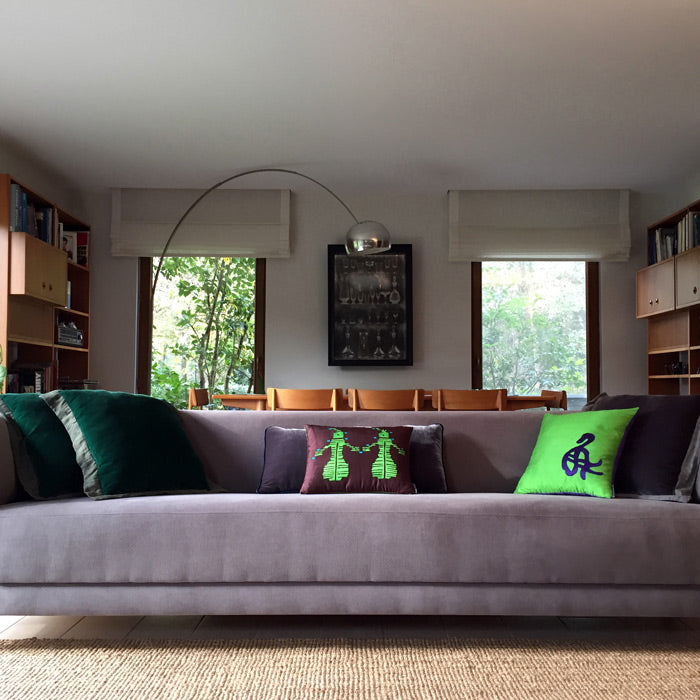 Salondaki gri uzun kanepede koyu yesil kadife ile desenli yesil ve kahverengi ipek yastiklar_Dark green velvet and patterned green and brown silk pillows on the gray long sofa in the living room