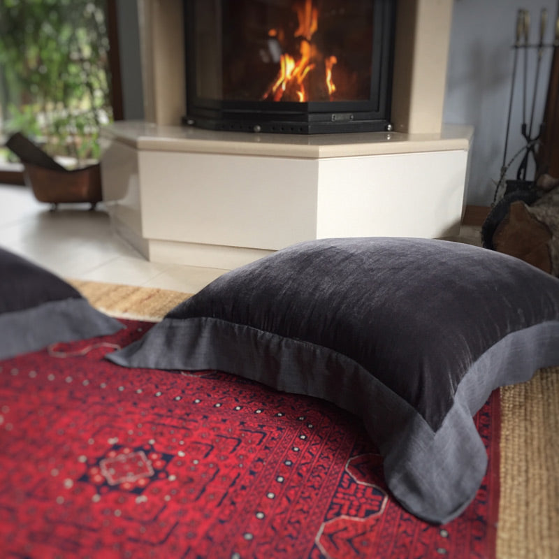 Sominenin onundeki bordo Afgan halisinin ustunde fume ipek kadife yer minderi_Smoke colored silk velvet floor cushion on a dark red Afghan carpet in front of the fireplace