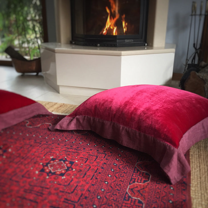 Sominenin onundeki bordo Afgan halisinin ustunde koyu kirmizi ipek kadife yer minderi_Dark red silk velvet floor cushion on a dark red Afghan carpet in front of the fireplace